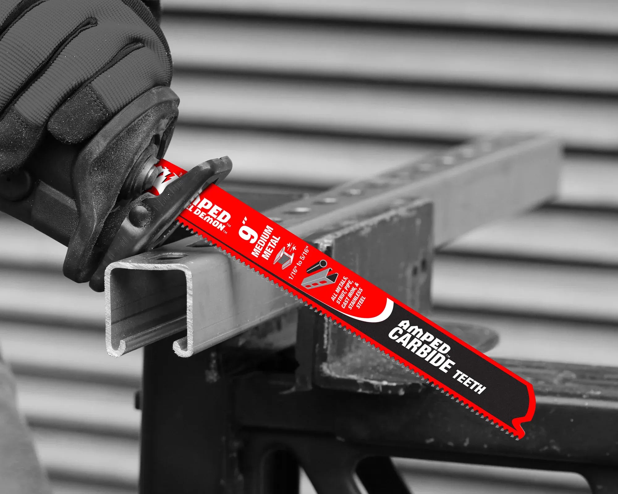 A close-up application photograph showing a gloved technician using a reciprocating saw equipped with a red Diablo AMPED medium metal carbide blade to cut straight down through a solid galvanized steel unistrut structural channel on a jobsite workbench.