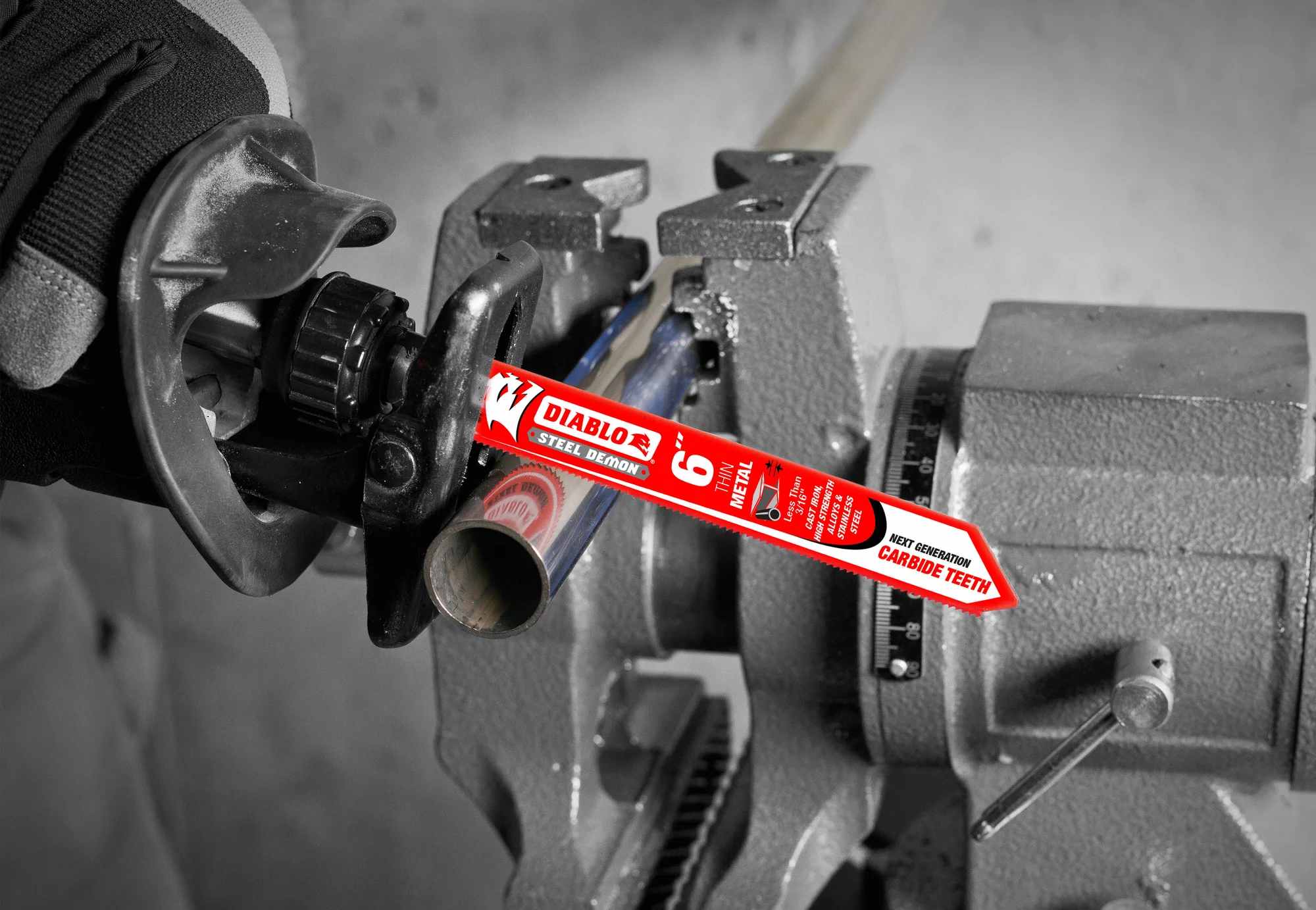 An action photograph of a 6 inch Diablo Steel Demon carbide blade in a reciprocating saw cutting through a thin-walled stainless steel pipe held in a bench vise, demonstrating the blade's precision and heat resistance in industrial metalwork.