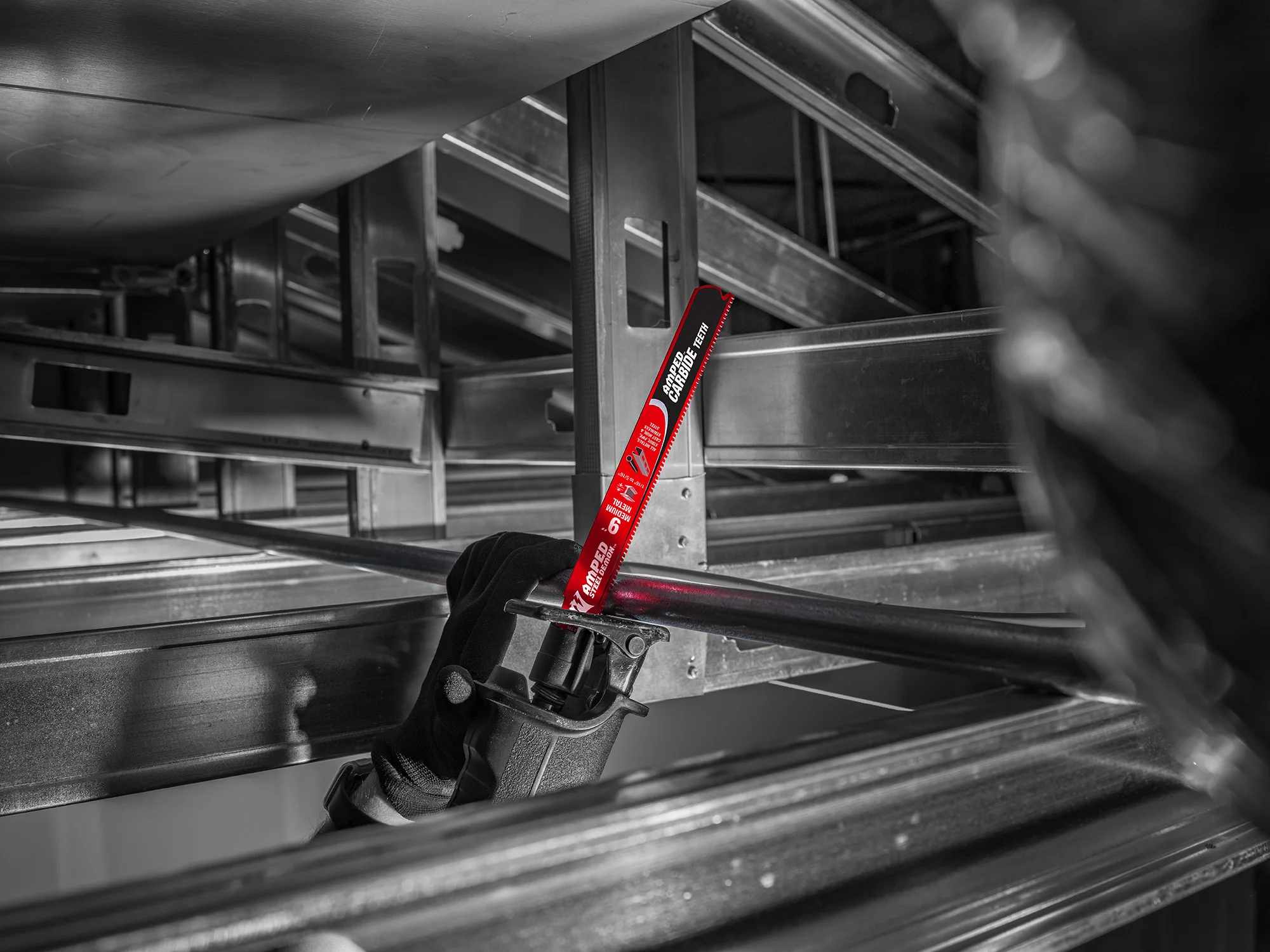 An action photograph of a 9 inch Diablo AMPED Steel Demon carbide blade in a reciprocating saw cutting through an industrial metal pipe in a tight overhead structural space, demonstrating the blade's precision and reach.