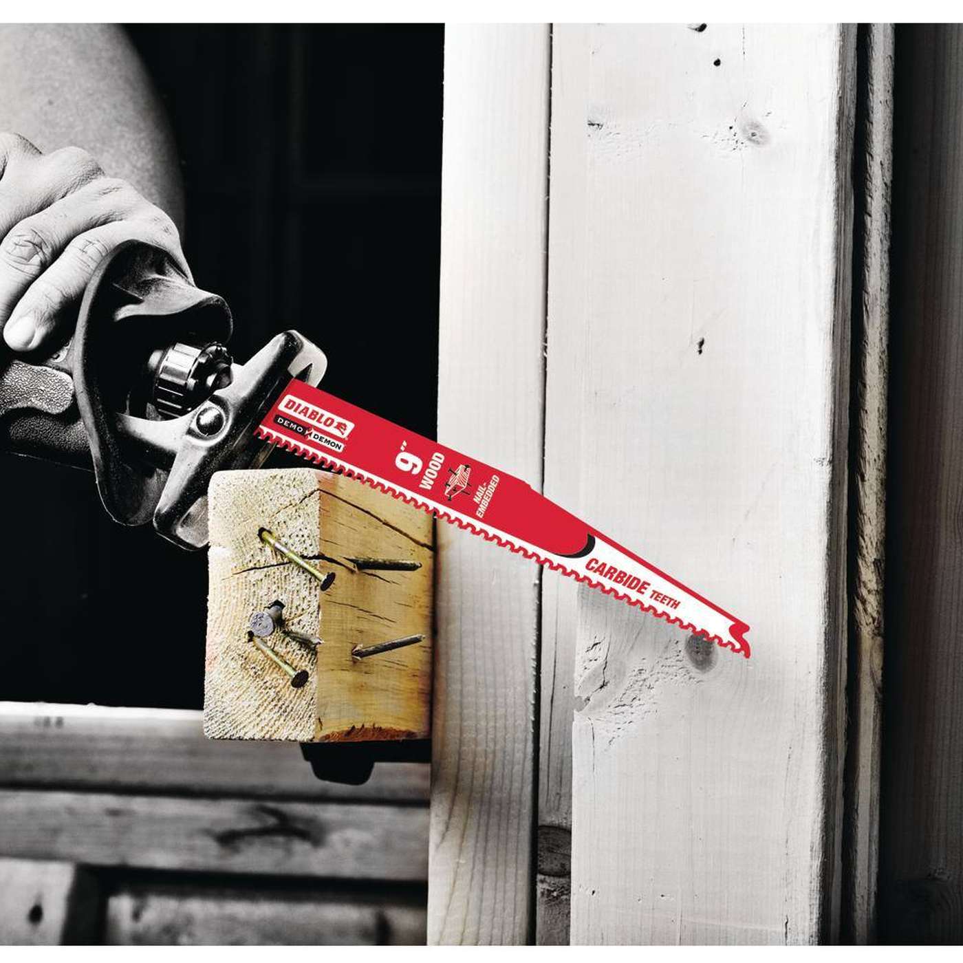 An action photograph showcasing a 9 inch red Diablo carbide teeth reciprocating saw blade as it slices through a wooden structural beam containing several large metal nails, illustrating the blade's precision and high-heat resistance in heavy-duty demolition.