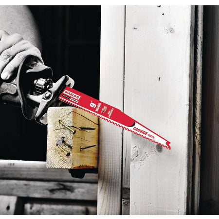 An action photograph showcasing a 9 inch red Diablo carbide teeth reciprocating saw blade as it slices through a wooden structural beam containing several large metal nails, illustrating the blade's precision and high-heat resistance in heavy-duty demolition.