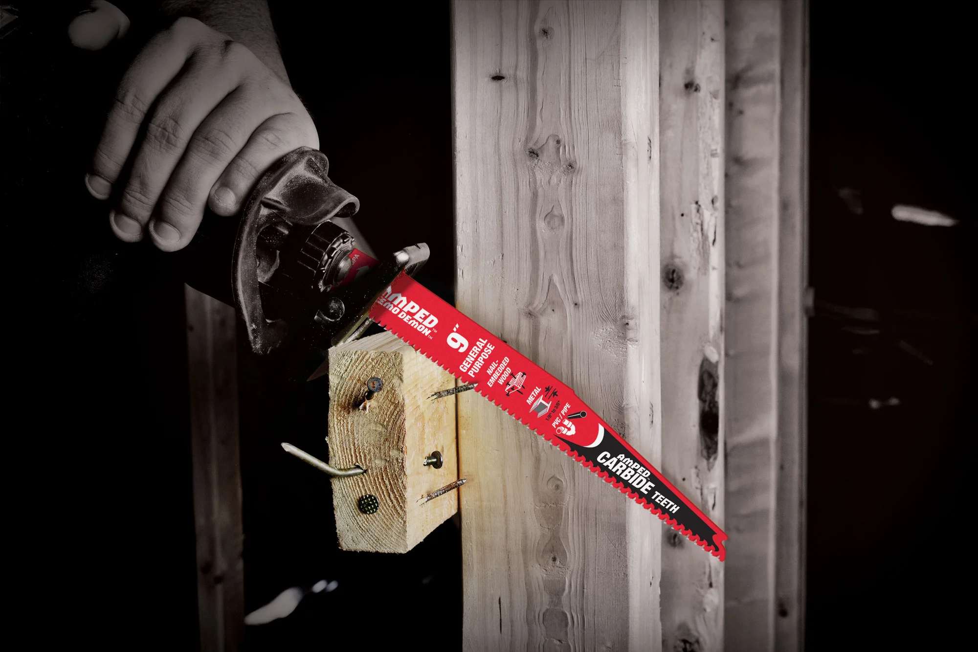 A close-up action photograph of the Diablo AMPED carbide blade as it slices through a wooden 2x4 stud embedded with metal nails, showcasing the impact resistance and aggressive cutting power of the variable 6/9 TPI tooth design.