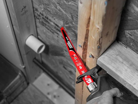 An action photograph of a 9 inch Diablo AMPED carbide blade in a reciprocating saw cutting through a wooden stud near a PVC pipe, demonstrating its precision in demolition tasks.