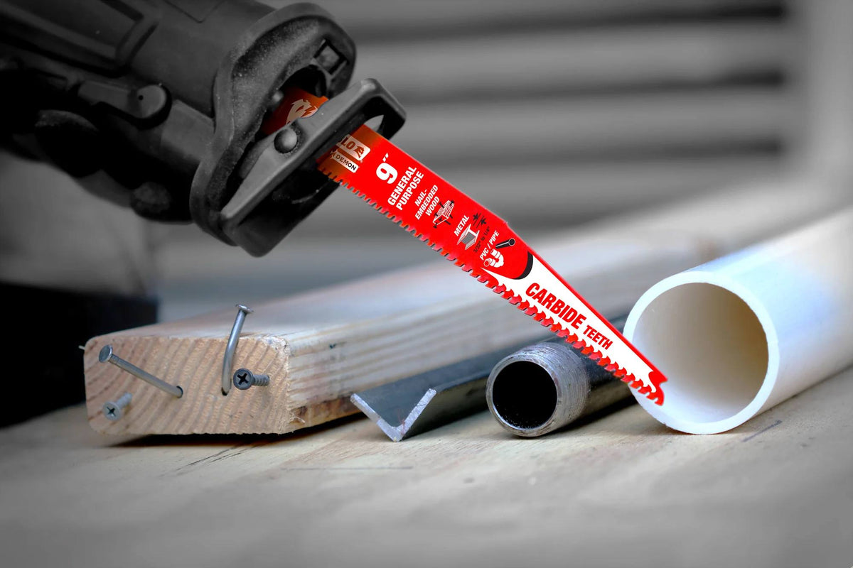 Action shot of a red Diablo Demo Demon 9 inch reciprocating saw blade with carbide teeth cutting through mixed materials including nail-embedded wood, metal pipe, and PVC conduit.