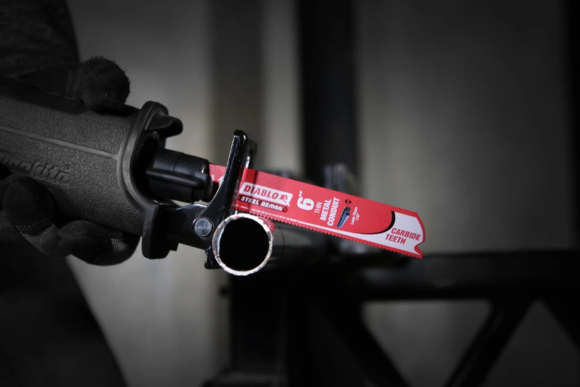 An action photograph of a Diablo Steel Demon carbide blade in a reciprocating saw cutting through a piece of industrial EMT conduit. The image demonstrates the blade's precision and ability to produce clean, burr-free cuts in thin-walled metal tubing.