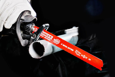 An action photograph of a Diablo Steel Demon 9 inch reciprocating saw blade cutting through a metal pipe held in place. The image showcases the red Perma-SHIELD coating and the blade's precise performance in thin-gauge metal cutting applications.