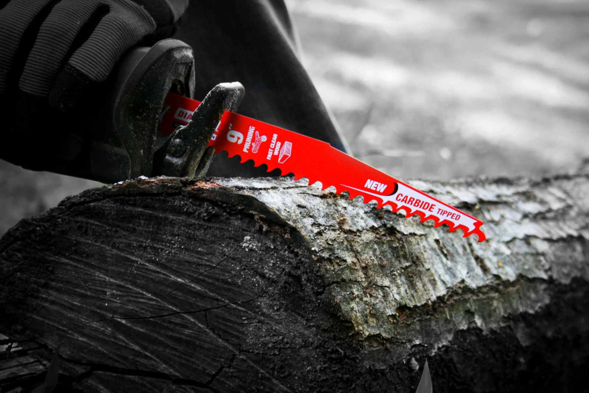 An action photograph of a Diablo 12 inch carbide pruning blade in a reciprocating saw slicing through a large fallen log. The image demonstrates the blade's aggressive material removal and efficiency during outdoor landscaping and storm cleanup.