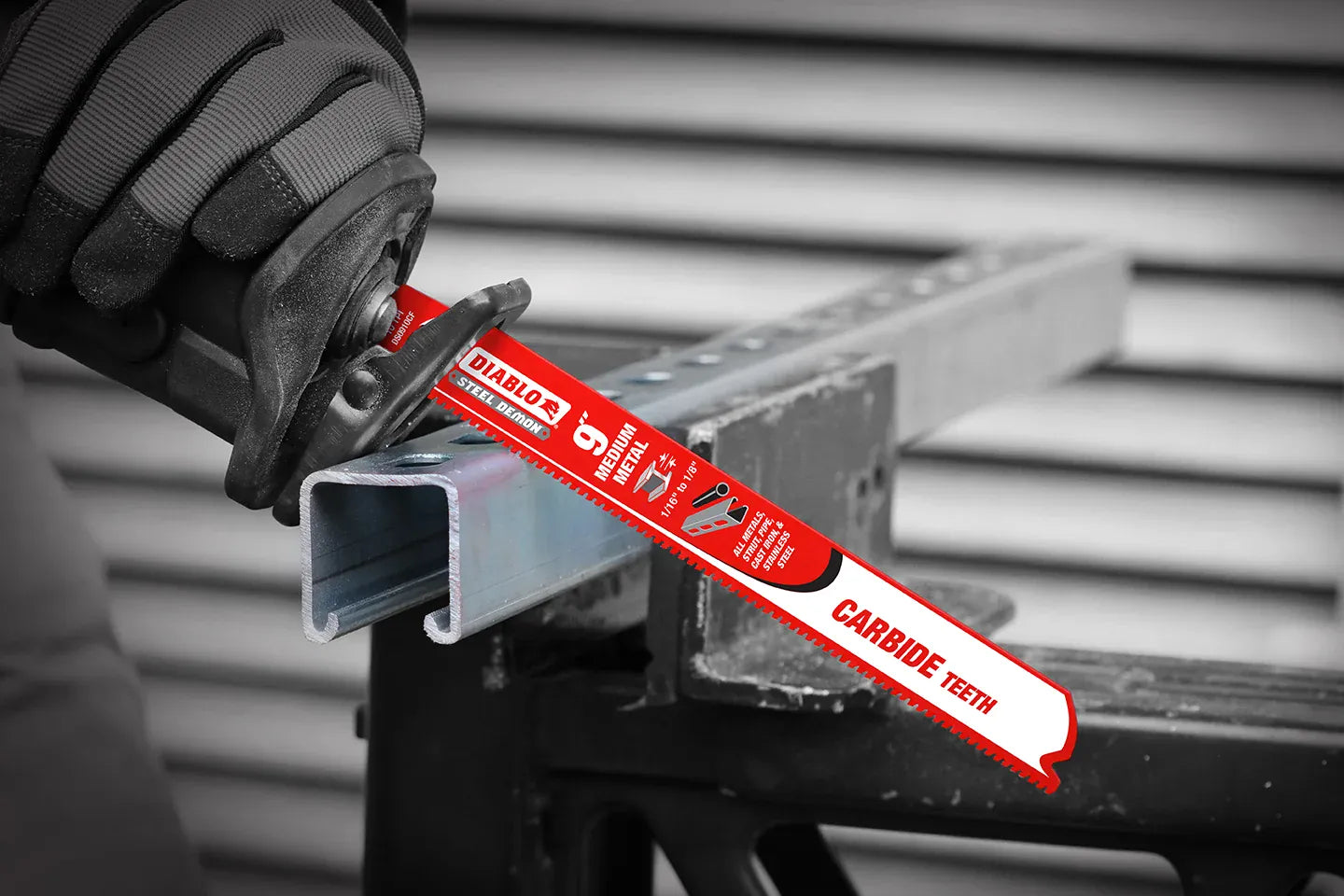 An on-site application shot of an operator using a cordless reciprocating saw equipped with a red Diablo Steel Demon carbide blade to execute a clean cross-cut through a heavy-duty galvanized steel unistrut channel clamped to a jobsite workbench.