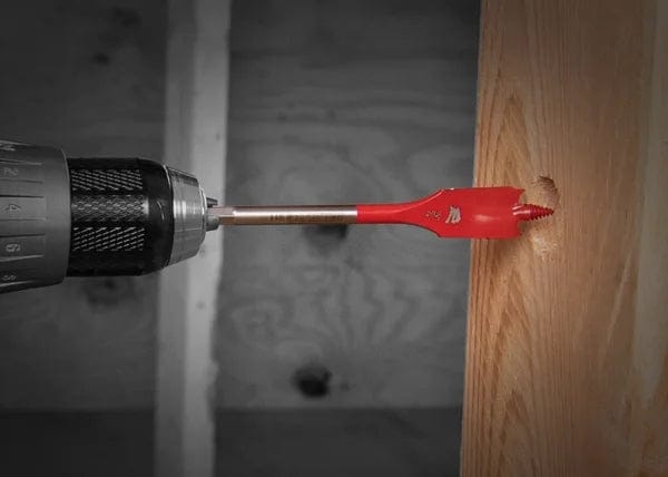An action photo of a red Diablo SPEEDemon spade bit attached to a cordless drill, demonstrating the self-feeding threaded tip engaging a wooden beam for high-speed hole boring.