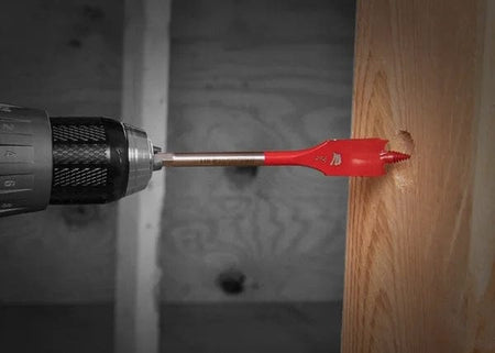 An action photo of a red Diablo SPEEDemon spade bit attached to a cordless drill, demonstrating the self-feeding threaded tip engaging a wooden beam for high-speed hole boring.