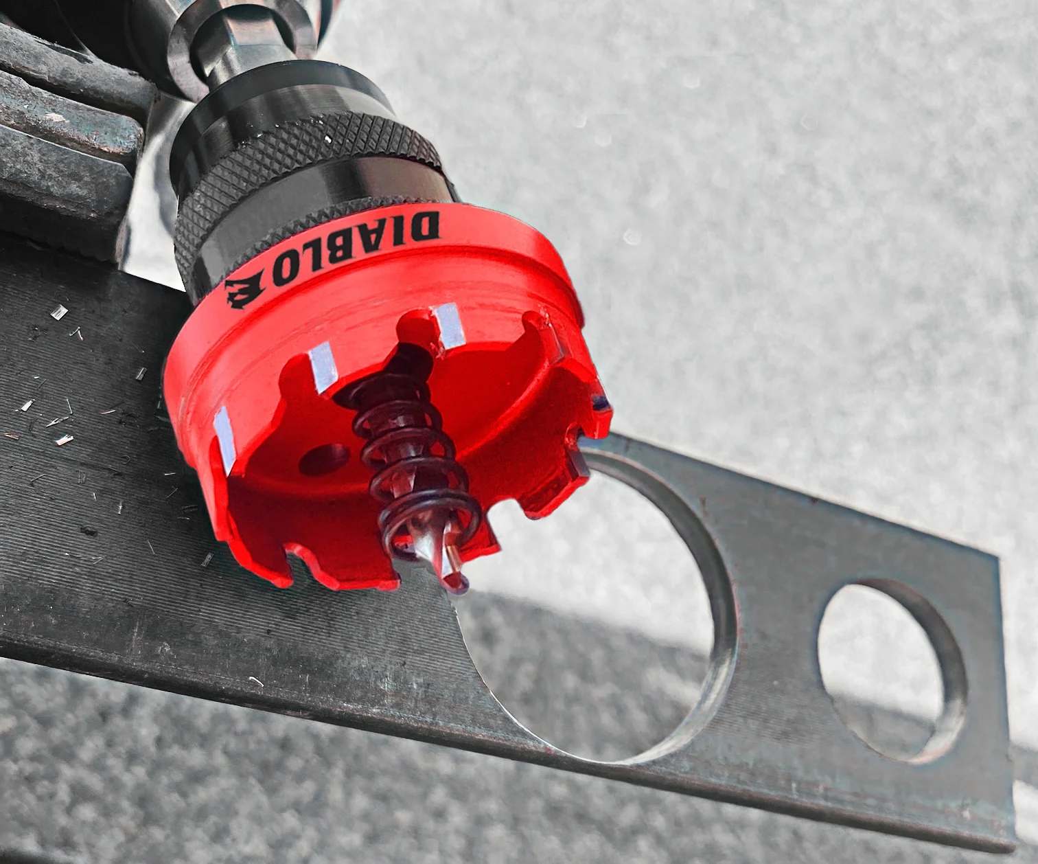 A selective-color action shot highlighting the red Diablo hole saw in a drill, having just completed a clean cut through a metal stud.