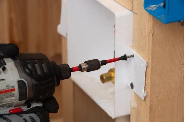 An action shot of a person using a cordless impact driver with a Diablo 3-1/2 inch PH2 drive bit to fasten a screw into a white metal plate mounted on a wooden stud.
