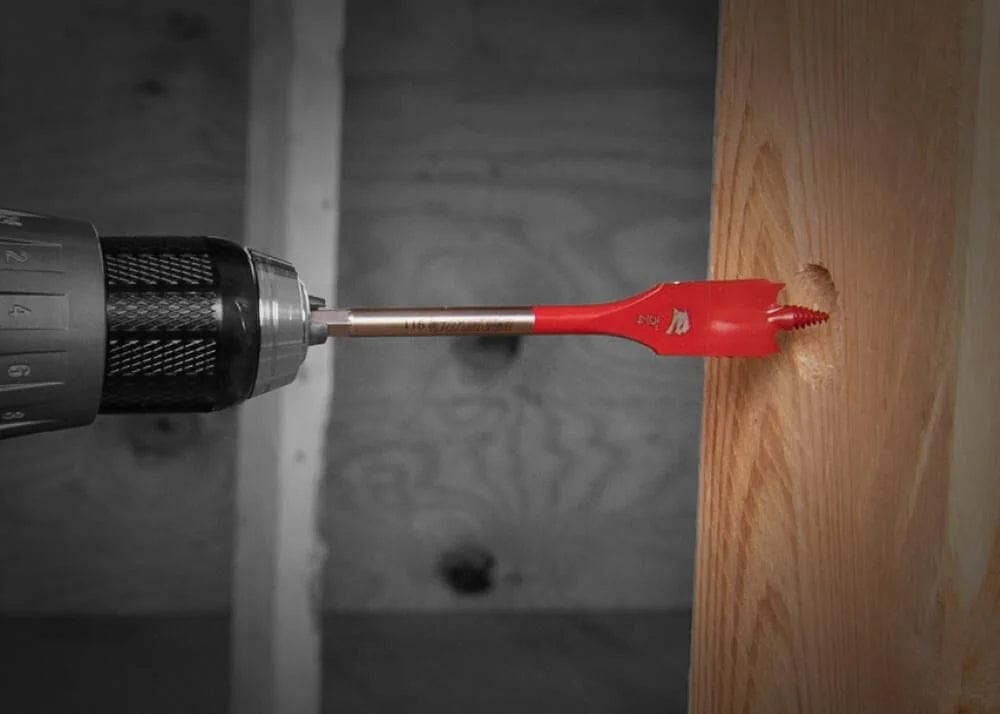 An application photo showing a red Diablo spade bit boring through a wooden stud, demonstrating the bit's ability to create clean, fast holes with a power drill.