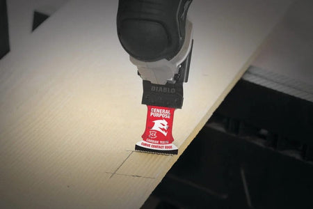 An action photo showing a Diablo carbide oscillating blade performing a precise plunge cut into a light-colored wooden board with marked lines.