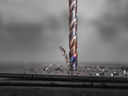 Close up of a Diablo Metal Demon drill bit penetrating a metal plate creating metallic shavings and demonstrating cutting precision