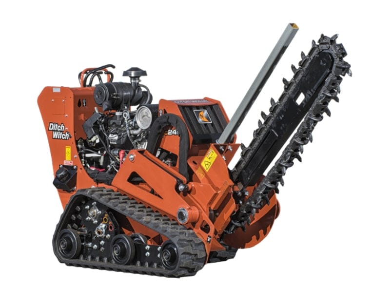 Close-up of Ditch Witch C24X walk-behind trencher showing trencher boom with digging teeth, rubber tracks, engine housing, and safety labels. Painted orange with visible branding, ideal for narrow trench excavation on varied terrain.