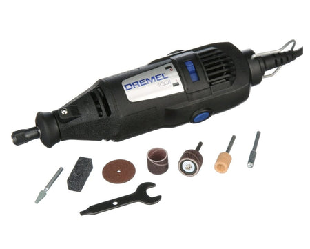 A studio shot of the Dremel 100 Series corded rotary tool, shown from a high angle with its 7 assorted accessories and the collet wrench laid out.