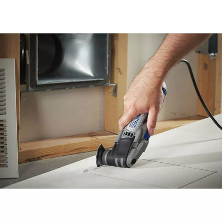 A hand guides the Dremel Multi-Max MM40 tool to make a rectangular plunge cut in a sheet of drywall.