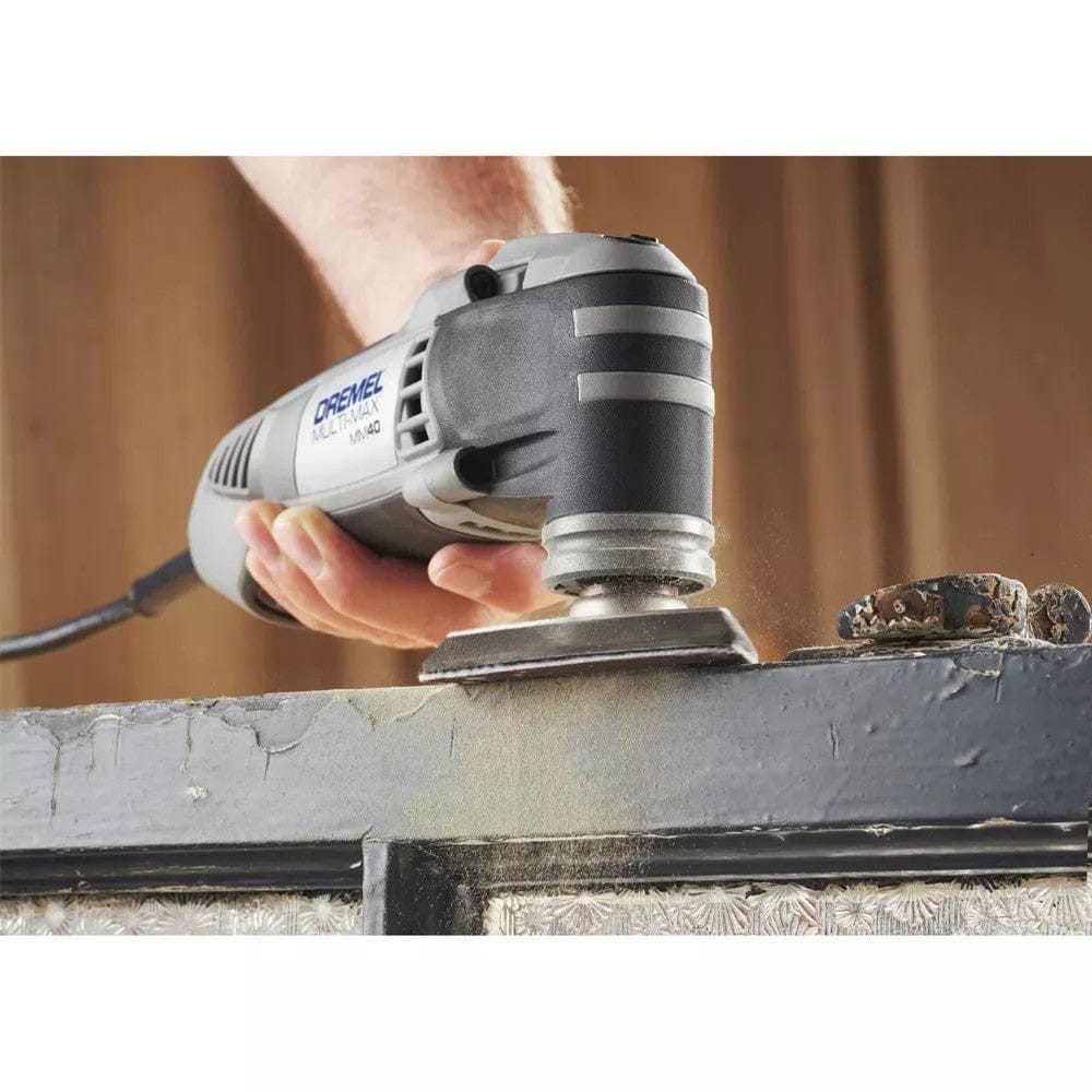 A hand holds the Dremel Multi-Max MM40 tool, using the sanding pad to sand peeling paint from a dark-colored window frame.