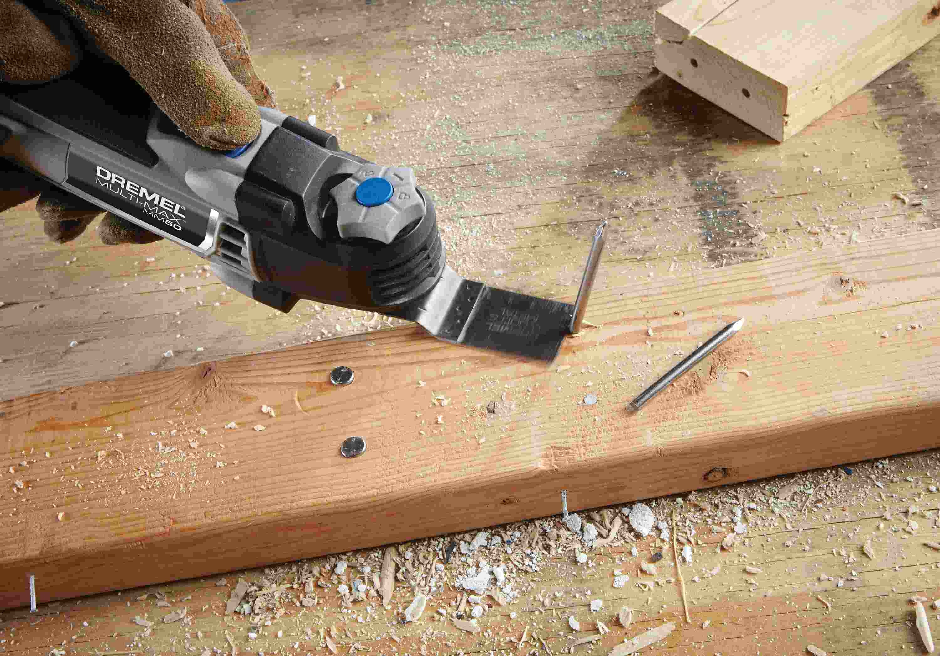 Lifestyle image demonstrating the Dremel MM50 oscillating multi-tool being used to trim a vertical PVC waste pipe flush with the subfloor next to a toilet.
