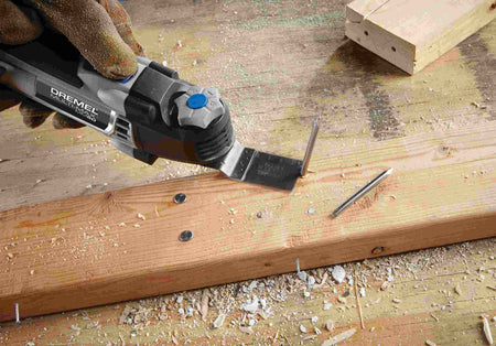 Lifestyle image demonstrating the Dremel MM50 oscillating multi-tool being used to trim a vertical PVC waste pipe flush with the subfloor next to a toilet.