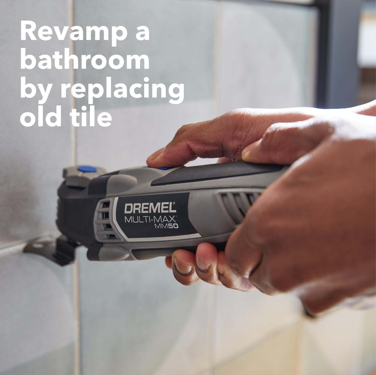 An application photo of a user using the Dremel MM50 multi-tool to plunge cut into a tiled bathroom wall, showcasing the tool's effectiveness for tile replacement and bathroom renovation.