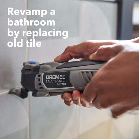 An application photo of a user using the Dremel MM50 multi-tool to plunge cut into a tiled bathroom wall, showcasing the tool's effectiveness for tile replacement and bathroom renovation.
