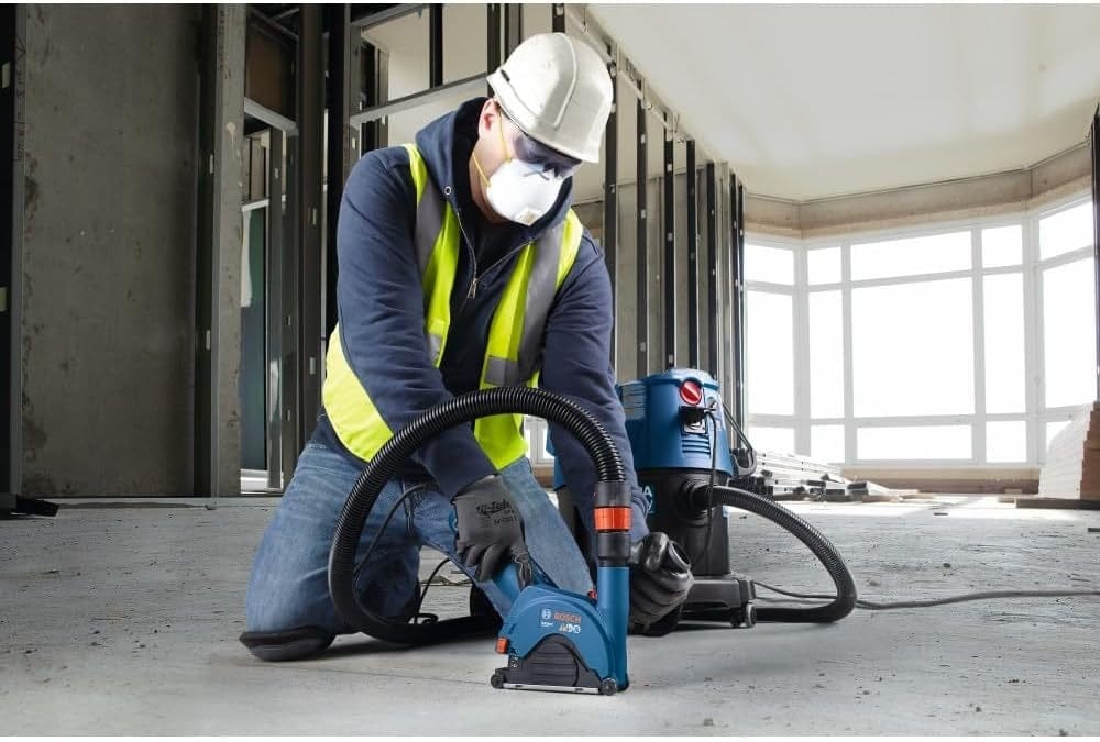 A person using a Bosch angle grinder and GA50DC dust collection shroud to make precise, dust-free cuts in an indoor concrete floor.