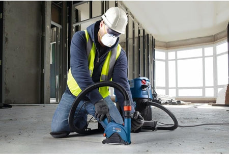 A person using a Bosch angle grinder and GA50DC dust collection shroud to make precise, dust-free cuts in an indoor concrete floor.