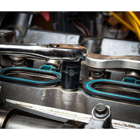 A mechanic using a chrome hand ratchet to loosen a bolt with a black E-Torx socket on a modern engine or housing, highlighting the tight clearance.