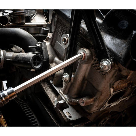 A long hex bit socket attached to an extension being used to access a deeply recessed bolt on a dirty car engine block.