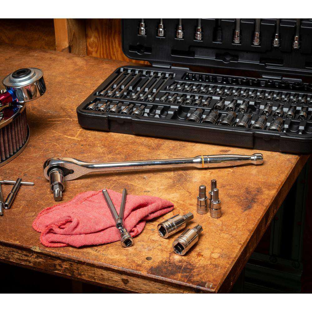 Various sockets and bits from the 80-piece set laid on a wooden workbench next to a long chrome ratchet, a red rag, and the open storage case.