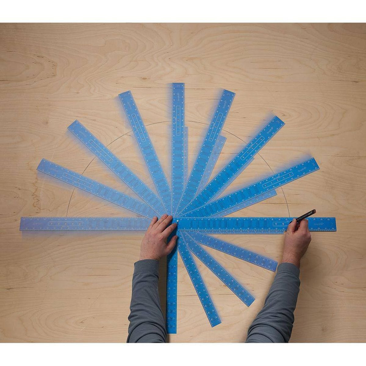 An overhead time-lapse application graphic showing a woodworker anchoring the heel point of the blue Empire framing square with a pin while rotating the blade arm across a sheet of smooth plywood, demonstrating how the system pivots smoothly to plot precise layout radial lines.