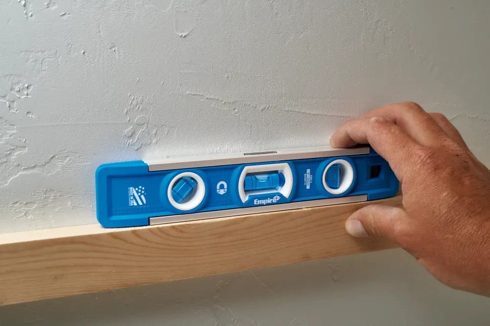 Lifestyle view of a user holding the magnetic torpedo level on a wooden surface against a textured wall to check for level during installation.