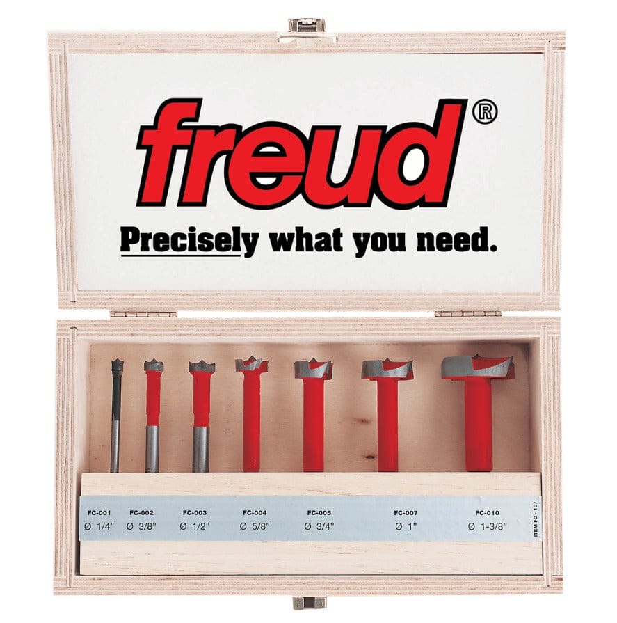 Freud FC-107 Forstner Bit Set displayed in an open wooden case. Includes seven red bits labeled with sizes from 1/4" to 1-3/8", each with silver cutting edges. Lid features Freud branding and slogan.