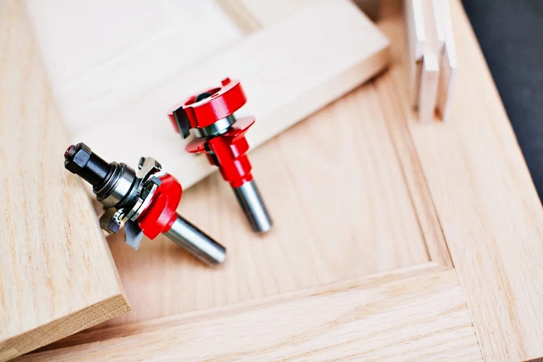 The Freud rail and stile router bits resting on a partially constructed wooden cabinet door in a workshop setting, showing the tools in a real-world application.