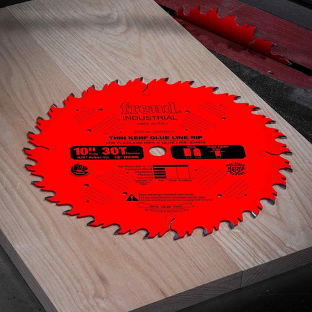 Action shot of a red Freud Glue Line Rip saw blade resting on a large hardwood slab, demonstrating industrial woodworking and joinery applications.