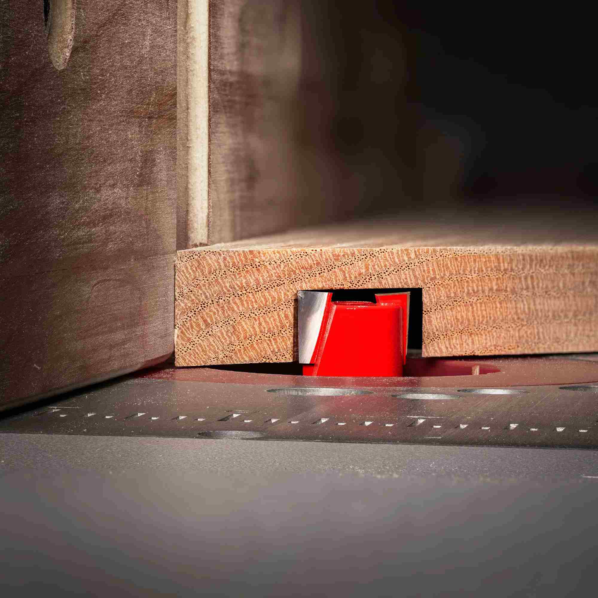 Close-up action shot of the red Freud 16-104 mortising router bit cutting a smooth, splinter-free dado in a piece of hardwood on a router table.