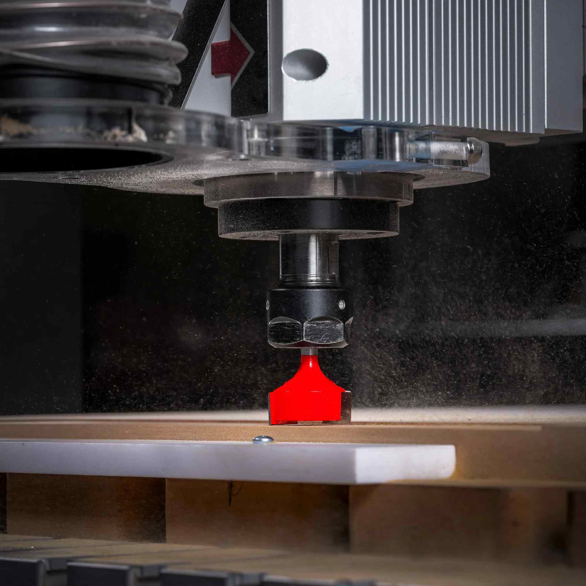 A high-performance CNC router machine in operation, showing the red Freud mortising bit surfacing a wooden board while creating fine wood dust.