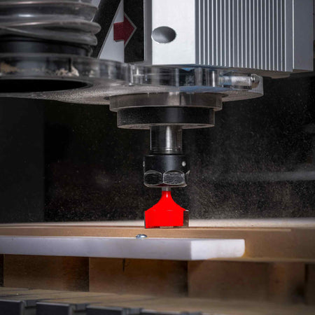 A close-up view of the Freud 16-108 mortising bit installed in a CNC router as it surfaces a wooden board, generating fine wood dust.