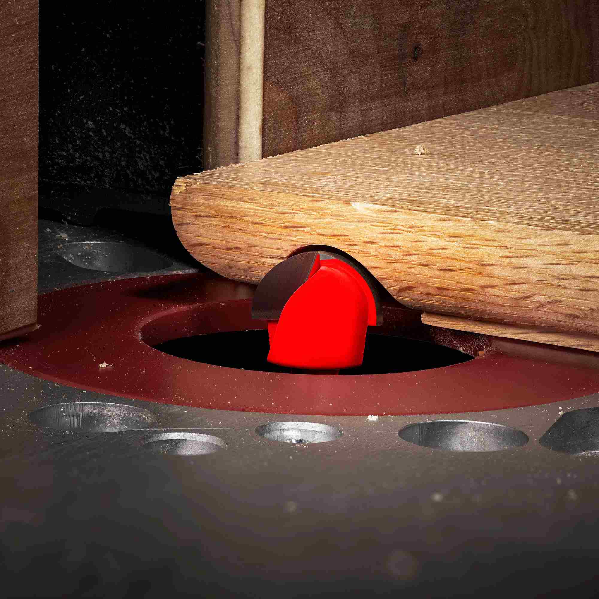 An action-oriented shot of a Freud round nose bit mounted in a table router, performing a decorative fluting cut on the surface of a wooden board.