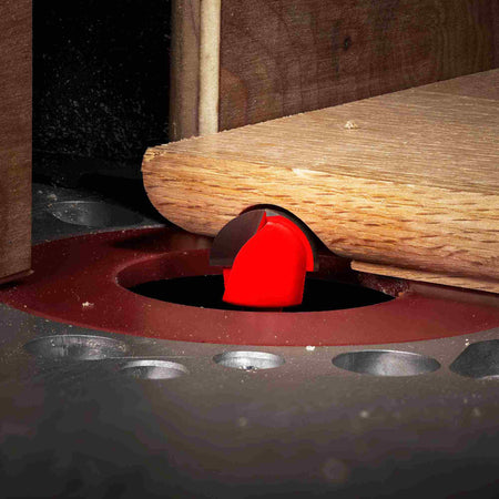 An action-oriented shot of a Freud round nose bit mounted in a table router, performing a decorative fluting cut on the surface of a wooden board.