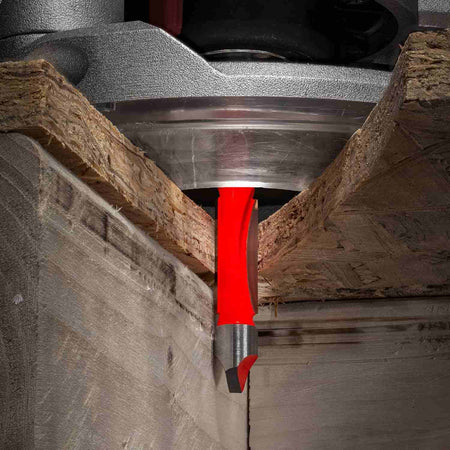 An action-oriented close-up of a Freud panel pilot bit plunging through a composite board, demonstrating its ability to self-start and guide along a template for precise cutouts.