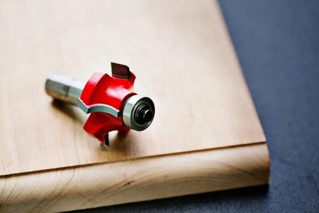 A high-angle photograph of the Freud 34-120 rounding over bit resting on a light-colored wooden board that has been routed with a matching 1/4 inch radius smooth edge.