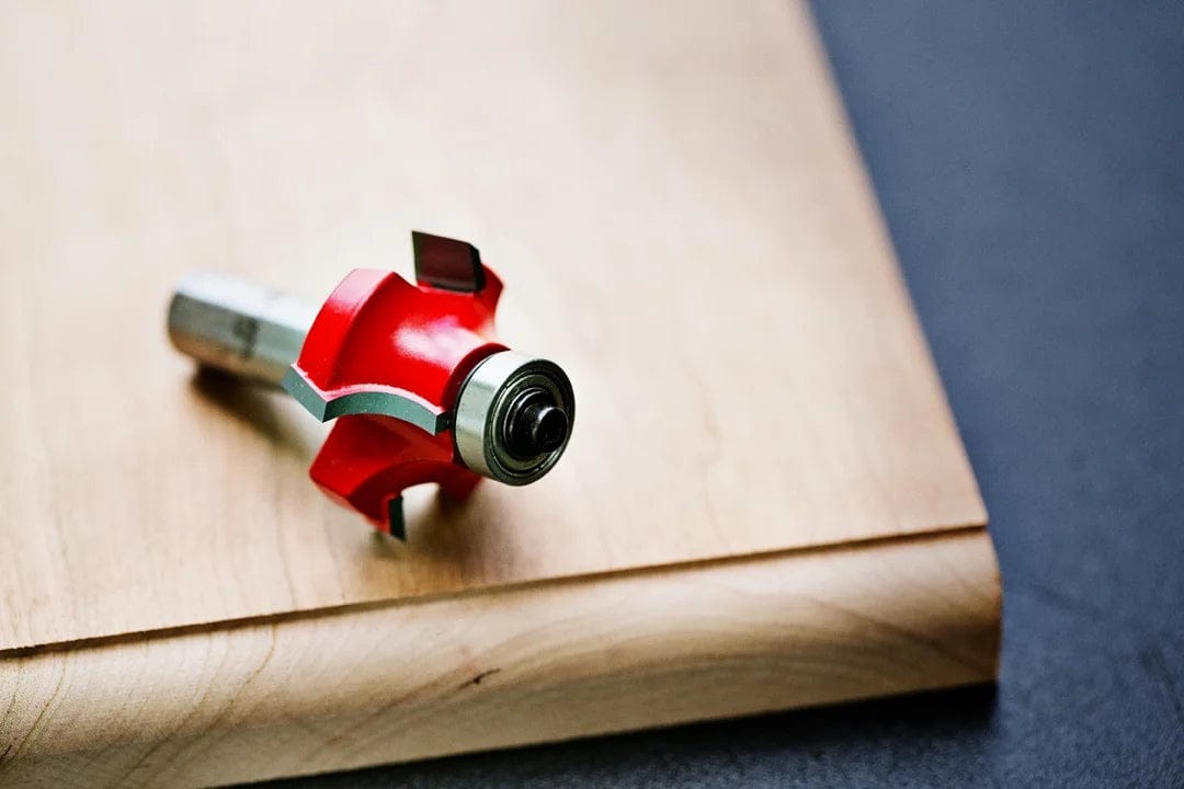 A high-angle photograph of the Freud 34-126 rounding over bit resting on a light-colored wooden board that has been routed with a matching 1/2 inch radius smooth edge.