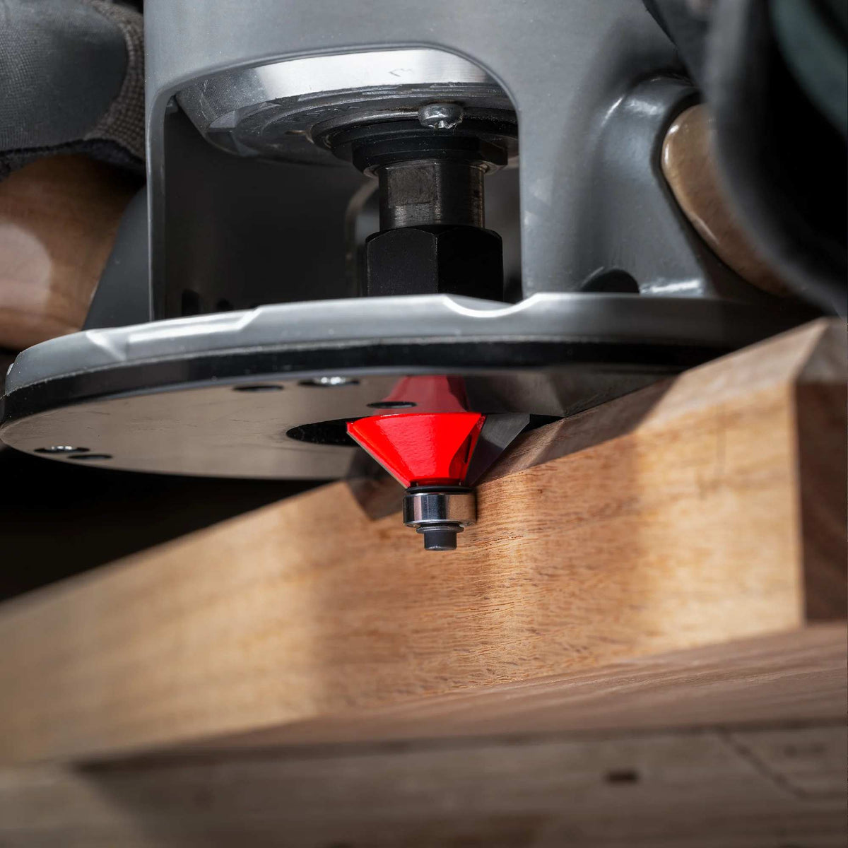 An action-oriented close-up of a Freud chamfer bit mounted in a plunge router, demonstrating the tool creating a crisp 25-degree bevel edge on a hardwood workpiece.