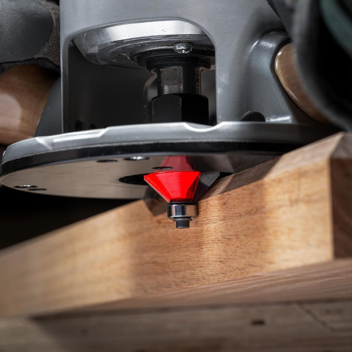 Action shot of a Freud 40-106 chamfer bit installed in a hand-held router, performing a clean 45-degree bevel cut on a hardwood board with the integrated guide bearing in use.