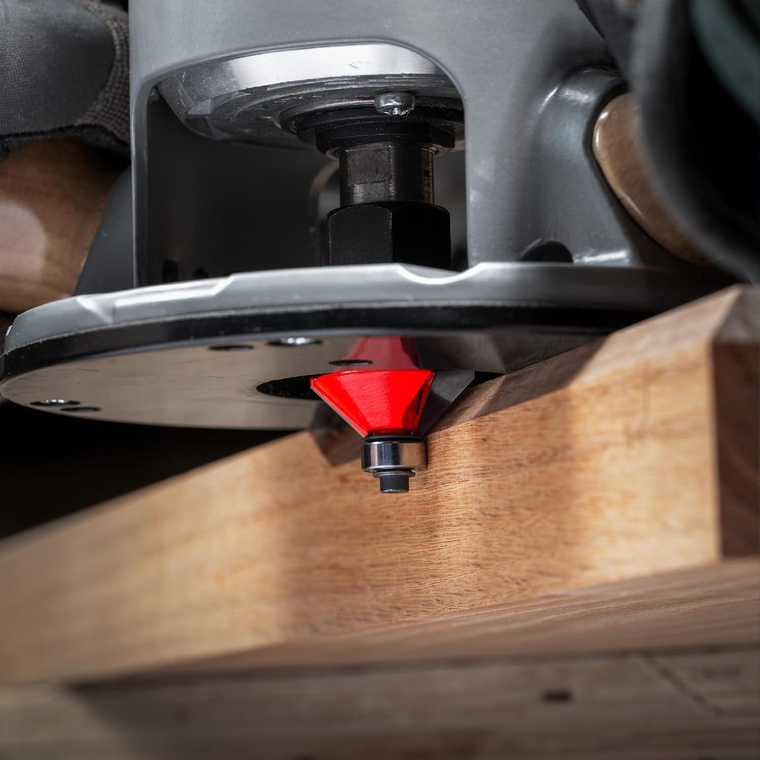 Action shot of a Freud 40-106 chamfer bit installed in a hand-held router, performing a clean 45-degree bevel cut on a hardwood board with the integrated guide bearing in use.