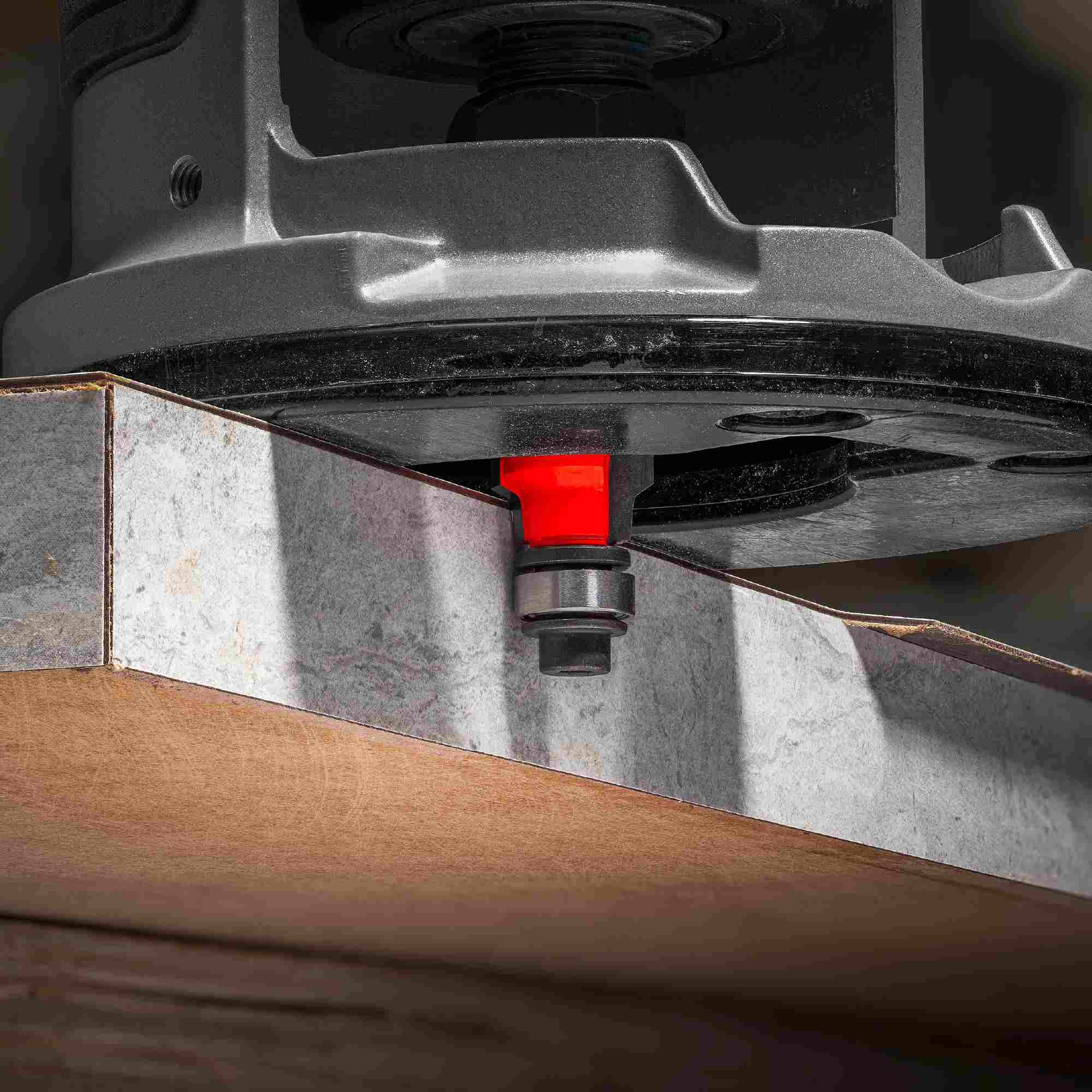 Close-up action shot of a hand-held router equipped with the red Freud 41-502 bit trimming a laminate edge flush and round on a workpiece.
