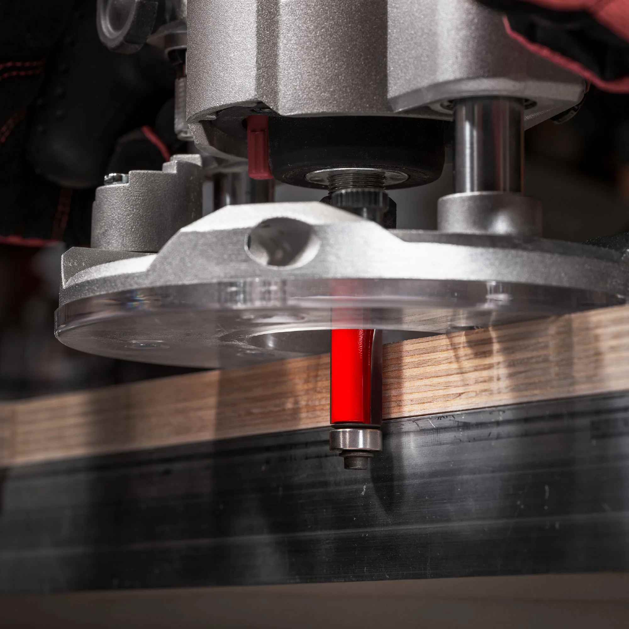 Close-up action shot of a hand-held router equipped with the red Freud 42-102 bit flushing the edge of a wooden board against a template.